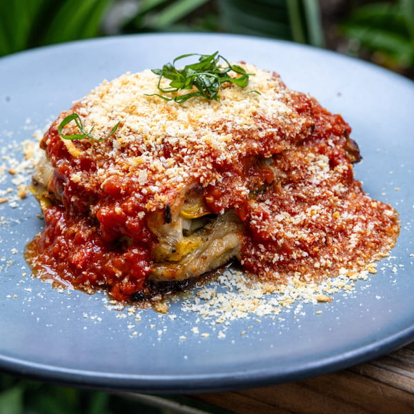 Fable's eggplant lasagna, topped with rich red sauce, grated cheese, and fresh herbs on a blue plate.