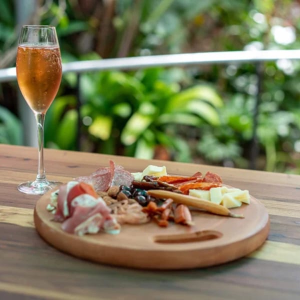 A glass of sparkling rosé and a charcuterie board with meats, cheeses, and olives on a wooden table.