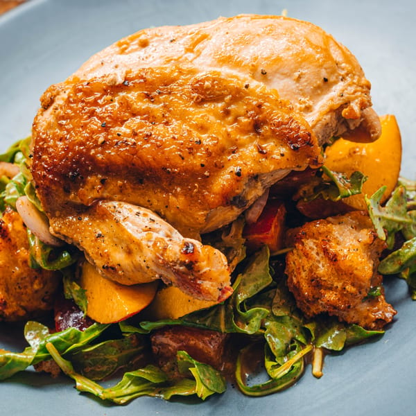 Crispy-skinned roasted chicken served over a bed of fresh greens, peaches, and croutons.
