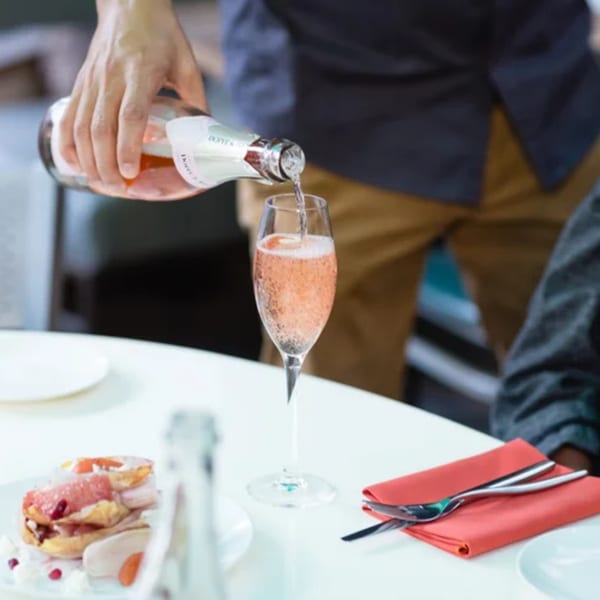 A hand pours sparkling rosé wine into a flute glass at a Fable restaurant table.