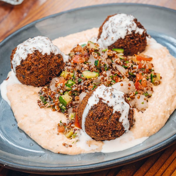 Three falafel balls with white sauce, served on a bed of hummus with quinoa salad.