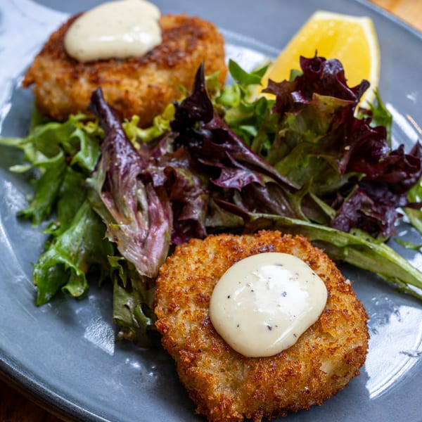 Two golden-brown Fable crab cakes topped with creamy sauce, served with fresh greens and a lemon wedge.