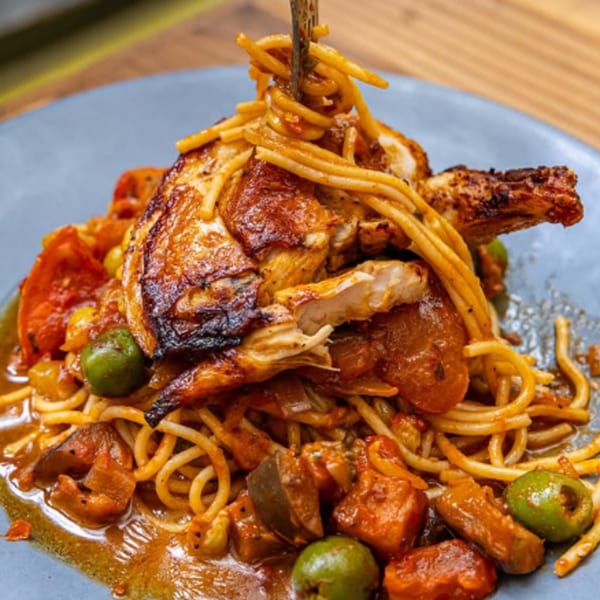 Fable's grilled chicken and spaghetti with tomato sauce and green olives on a blue plate.