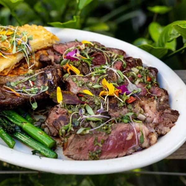 Fable's sliced steak with chimichurri, hash browns, and broccolini, garnished with edible flowers.