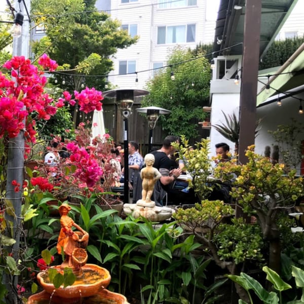 Fable's outdoor patio with diners, lush pink bougainvillea, and decorative fountains.
