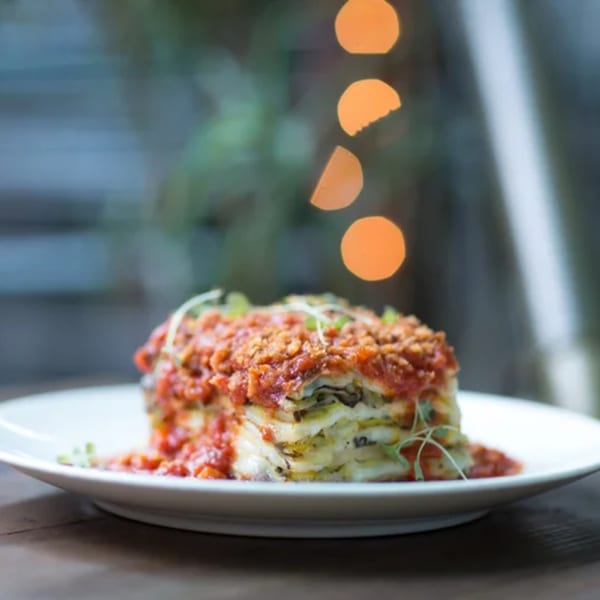 Fable's layered lasagna with rich red sauce and microgreens on a white plate.
