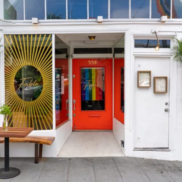 The Fable restaurant's white storefront with a red door, outdoor seating, and sunburst window decal.
