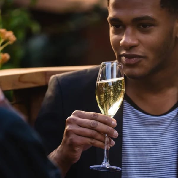 A man in a striped shirt and dark jacket holds a glass of sparkling wine at Fable.