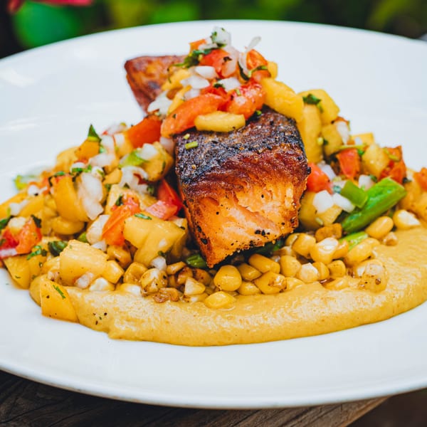 Pan-seared salmon with corn, pineapple salsa, and a yellow puree on a white plate.