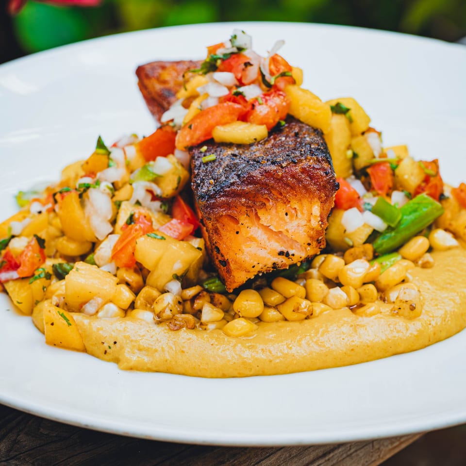 Pan-seared salmon with corn, pineapple salsa, and a yellow puree on a white plate.